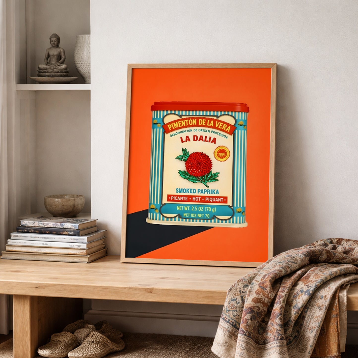 Framed Spanish Smoked Paprika Tin print styled on a shelf with folded textiles and simple decor in a neutral room. The artwork adds a bright orange accent and shows the full vintage paprika tin design with Spanish text, blue stripes and red floral detail. Accurate for searches around Spanish kitchen wall art, retro pantry decor, Mediterranean food art and framed cultural wall decor.