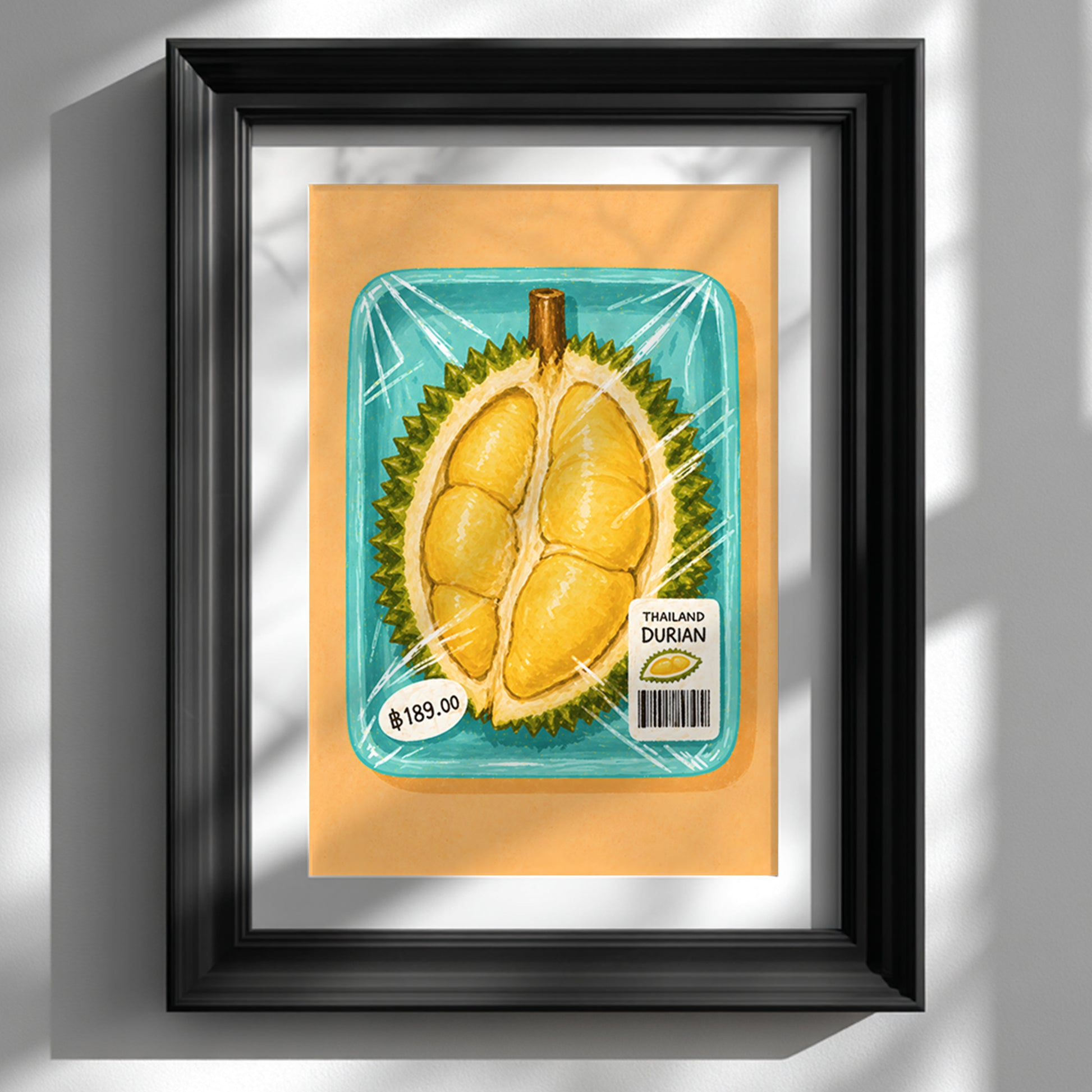 Thai durian market art print showing packaged yellow durian in a turquoise tray, displayed in a deep black frame with a white mount on a sunlit wall.