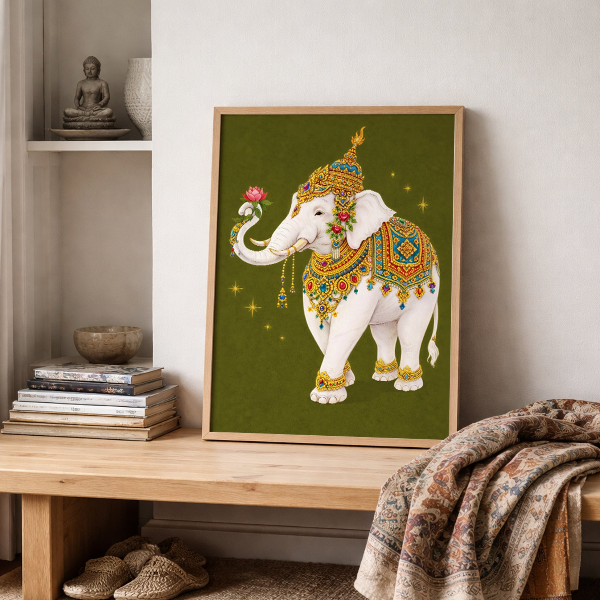 Thai royal white elephant wall art leaning on a wooden shelf with folded textured fabrics and neutral décor. The sacred elephant features ornate gold detailing, colourful Thai-inspired patterns and a lotus flower in its trunk. The olive green background and soft natural light highlight the traditional royal symbolism within a contemporary cultural interior setting.