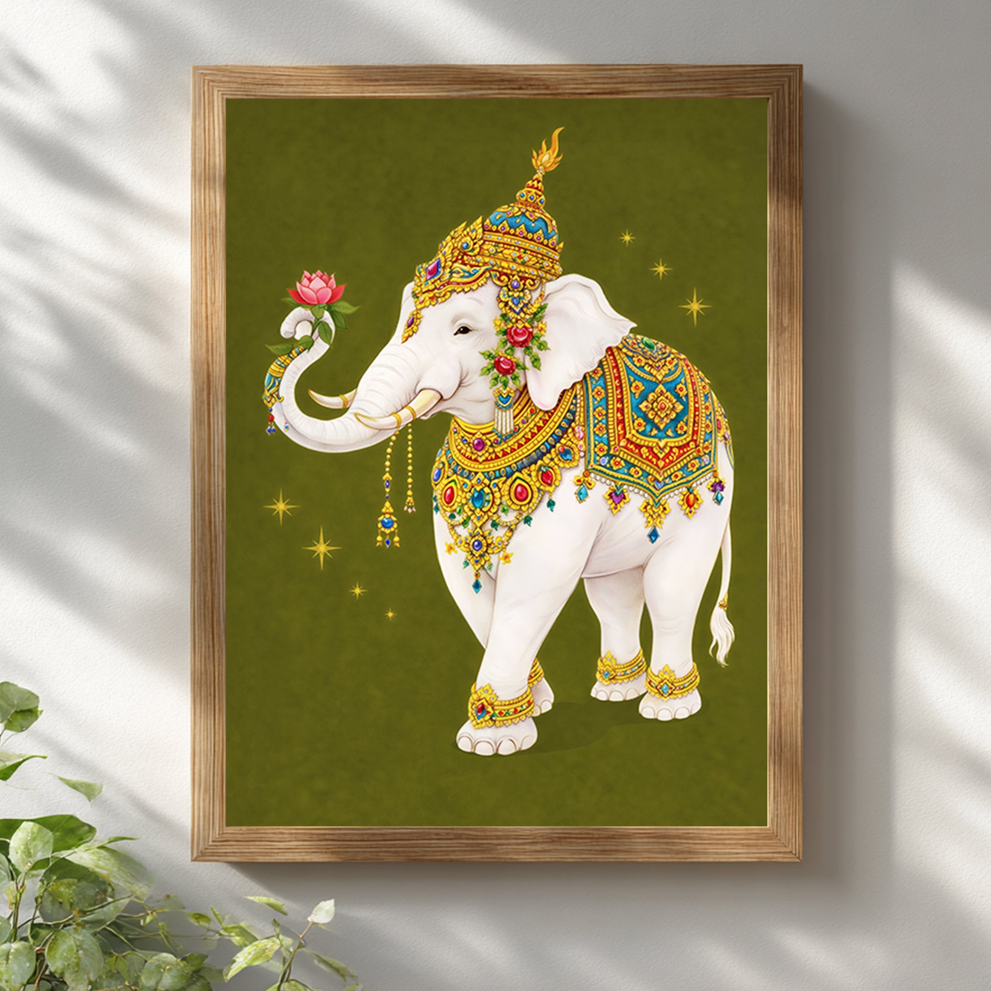 Thai royal white elephant wall art presented in a light wooden frame against a white wall. The sacred white elephant is richly adorned in gold and colourful Thai royal regalia, holding a pink lotus flower. The olive green background contrasts with the natural wood frame, creating a balanced blend of traditional Thai symbolism and minimalist interior styling.