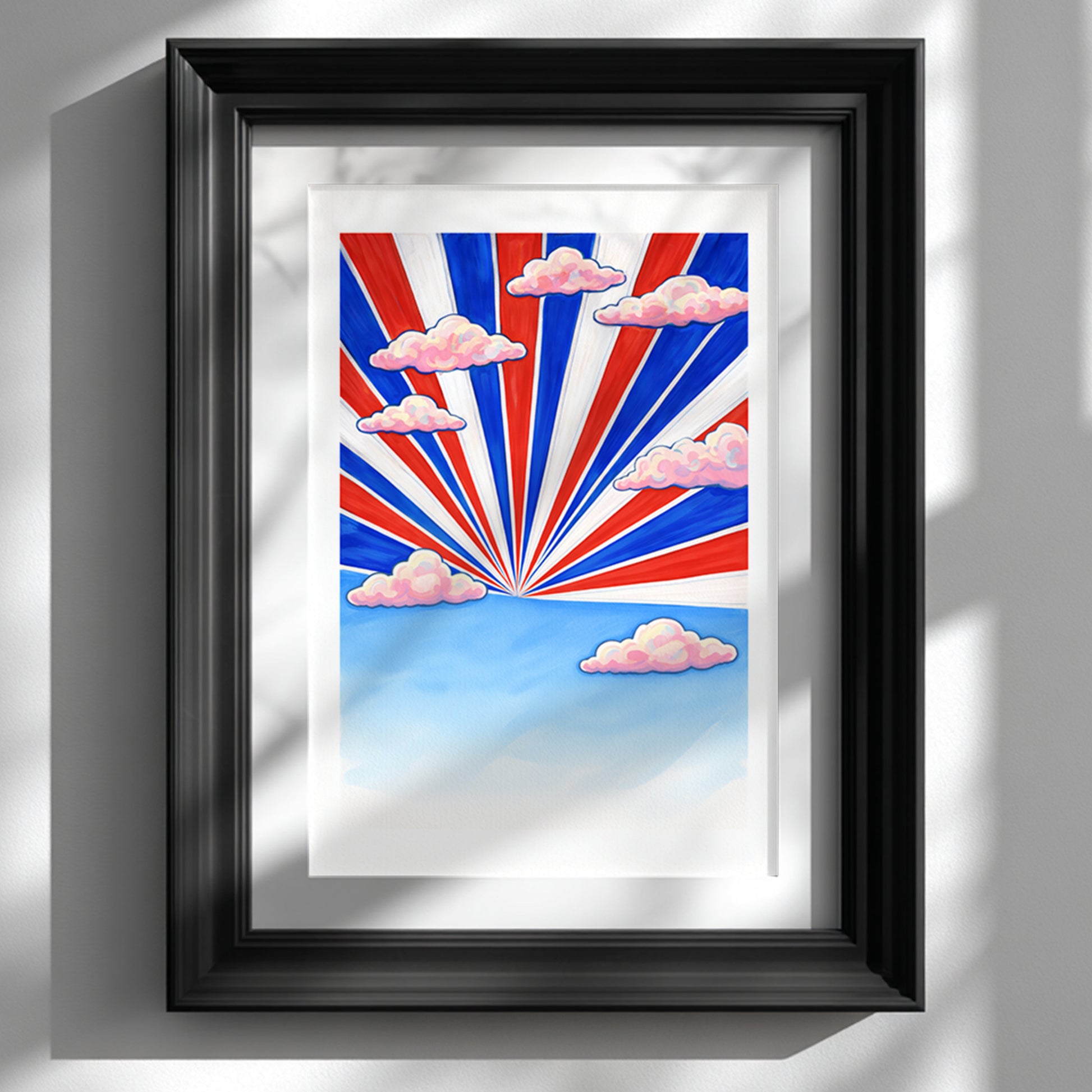 Framed Thai Sky Sunburst Thailand travel poster in a black frame on a white wall. Red, white and blue rays inspired by the Thai flag radiate from a central sun point across a clear blue sky with soft pink clouds. Modern Southeast Asia wall art styled as bold graphic decor for a living room or home office.