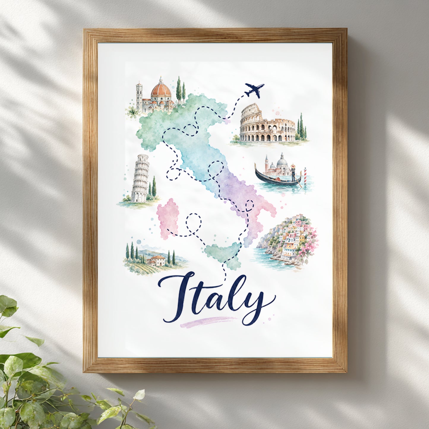 Italy watercolour map poster displayed in a light wooden frame on a clean white wall, with soft window shadows and blurred green leaves in the foreground. The artwork combines pastel map colours, dotted travel routes, a small aeroplane, Italian landmarks and bold Italy lettering for bright Mediterranean-inspired wall decor.