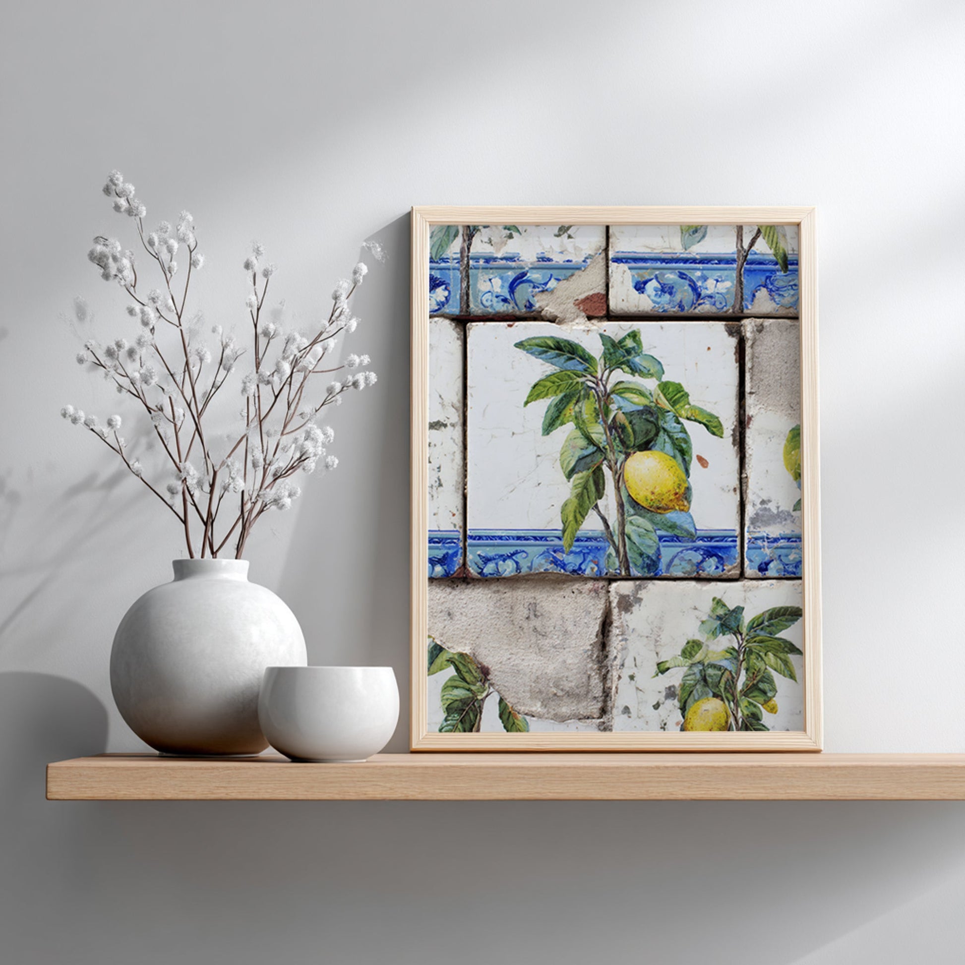 Portuguese lemon azulejo print in a light wooden frame on a white wall, showing yellow lemons, green foliage and distressed blue-and-white tile details.