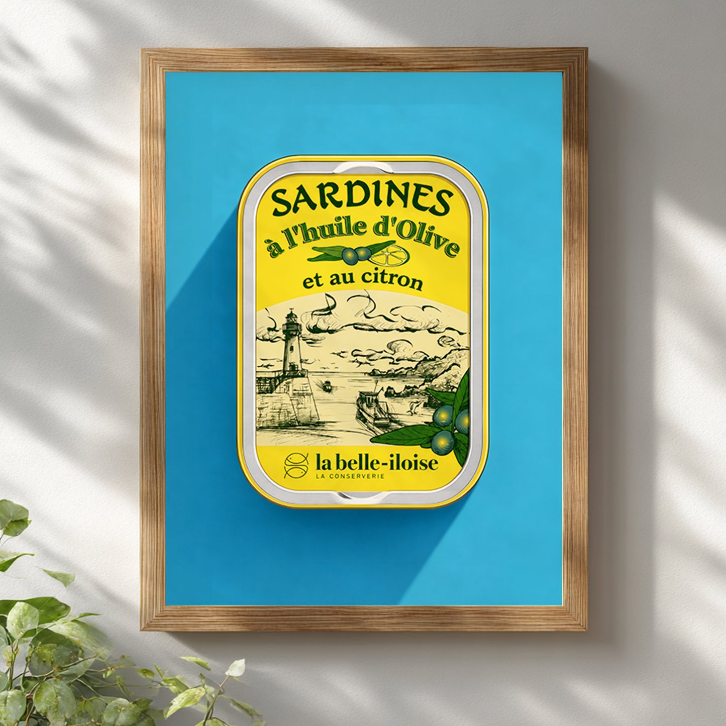 French sardine tin pop art print displayed in a light wooden frame on a white wall, featuring turquoise blue and yellow vintage food packaging artwork beneath soft natural leaf shadows.